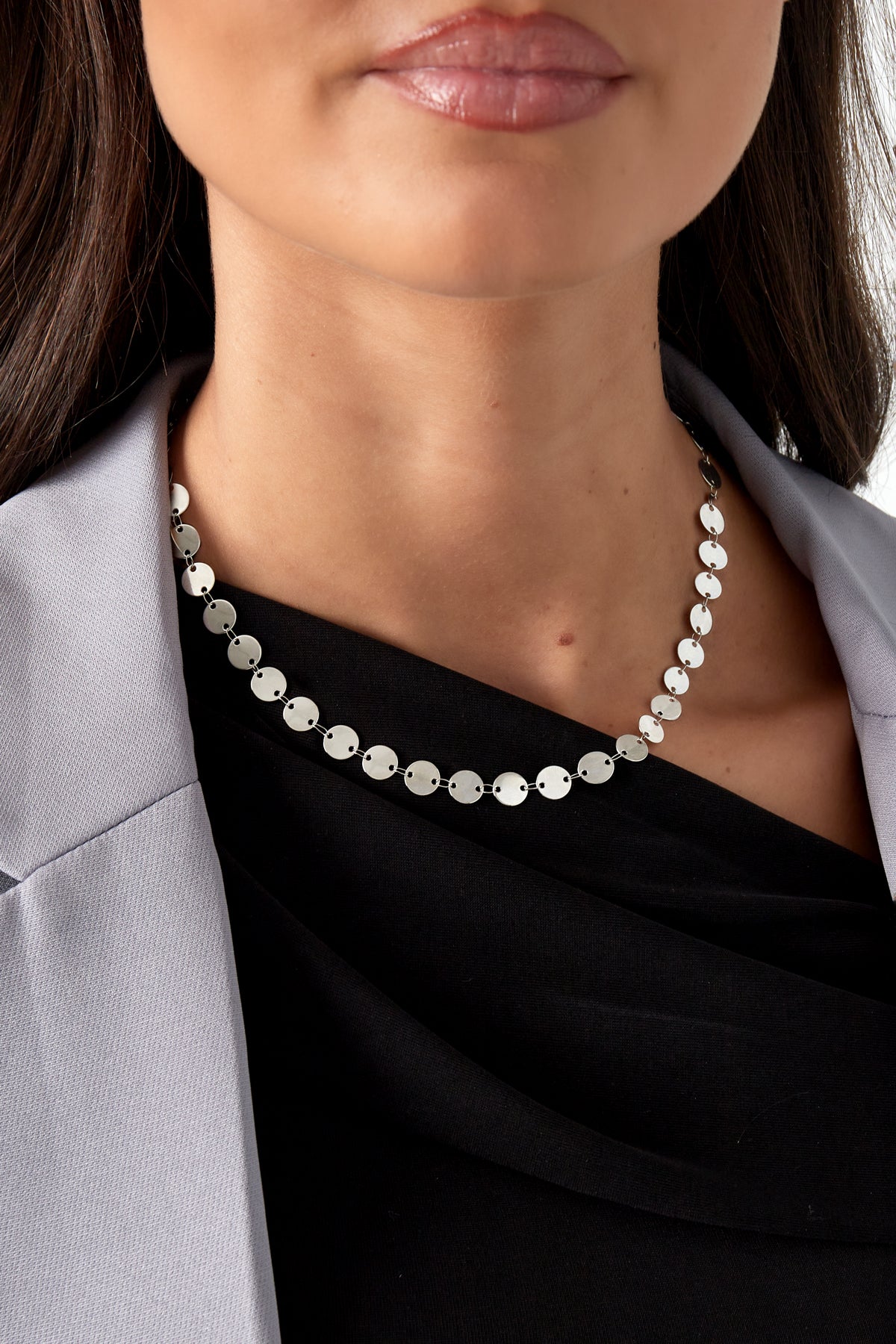 Model wearing a silver-toned disc chain necklace styled with a black top and gray blazer showcasing a youthful, boutique look.