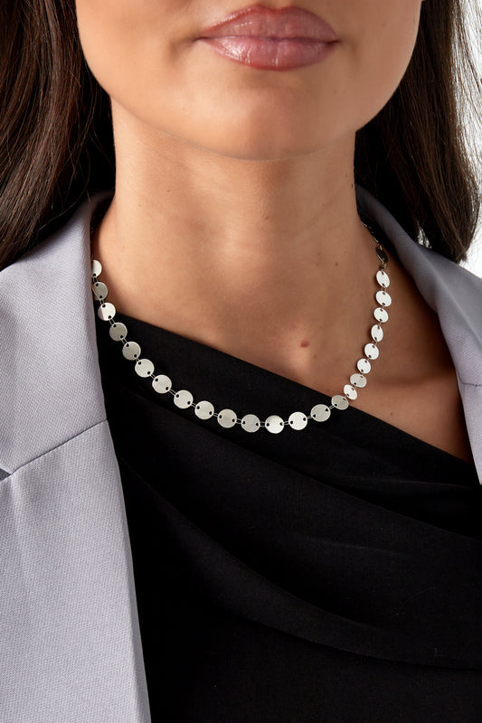 Model wearing a silver-toned disc chain necklace styled with a black top and gray blazer showcasing a youthful, boutique look.