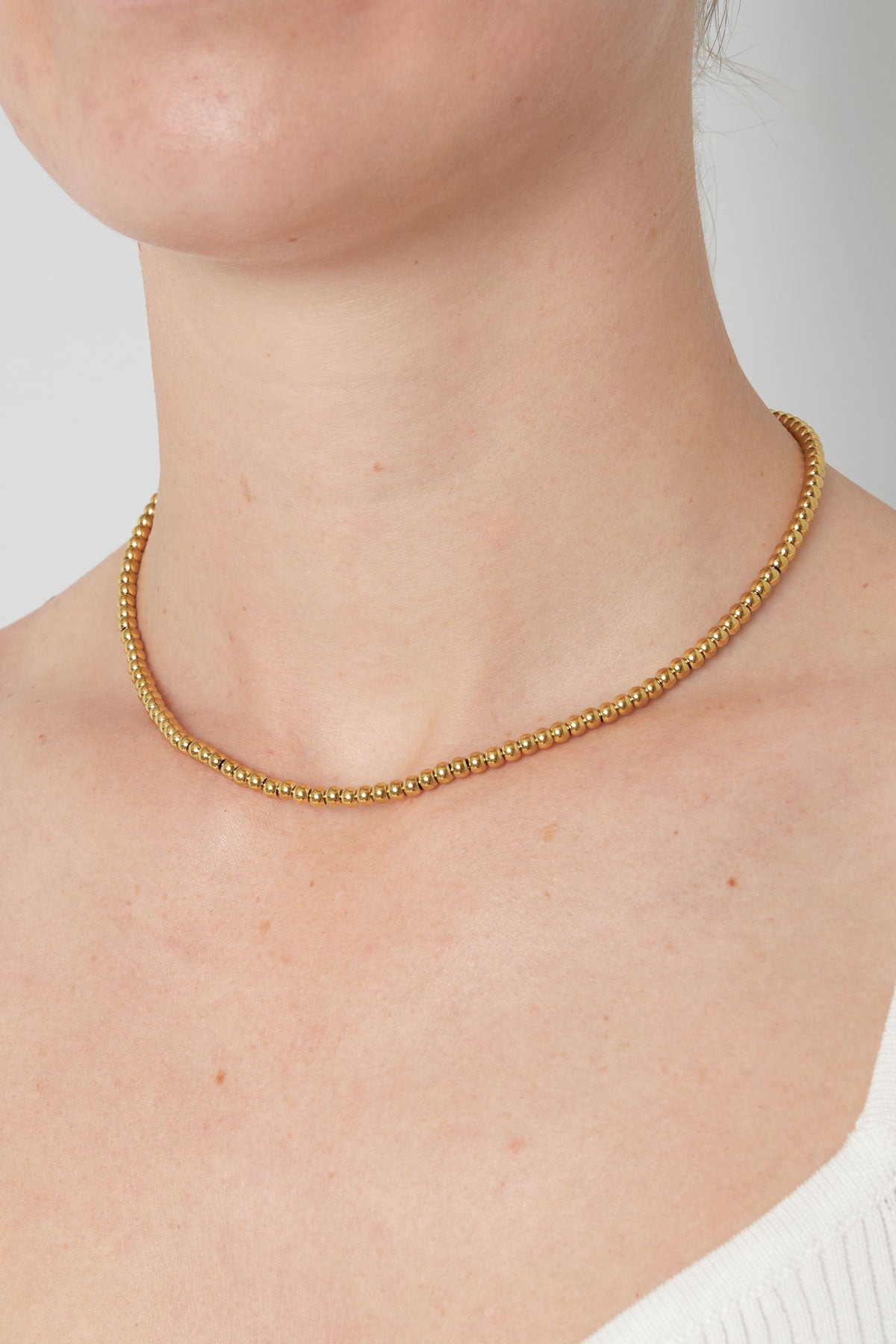 Gold-toned beaded necklace worn around a woman's neck highlighting its minimal and elegant design