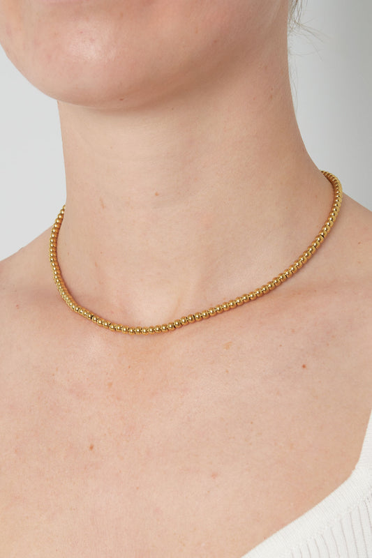 Gold-toned beaded necklace worn around a woman's neck highlighting its minimal and elegant design