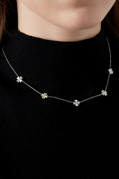 Close-up of silver tone four-leaf clover necklace worn on woman with black top