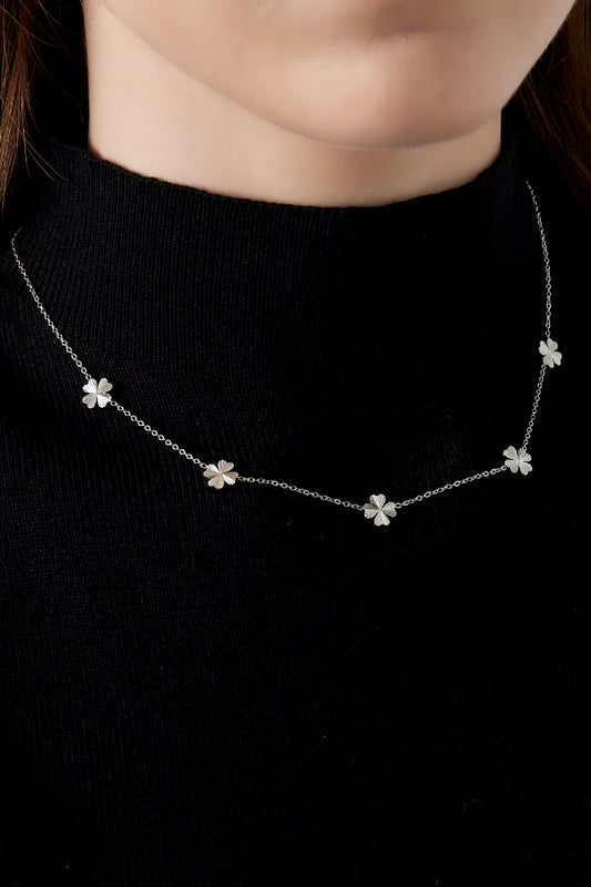 Close-up of silver tone four-leaf clover necklace worn on woman with black top