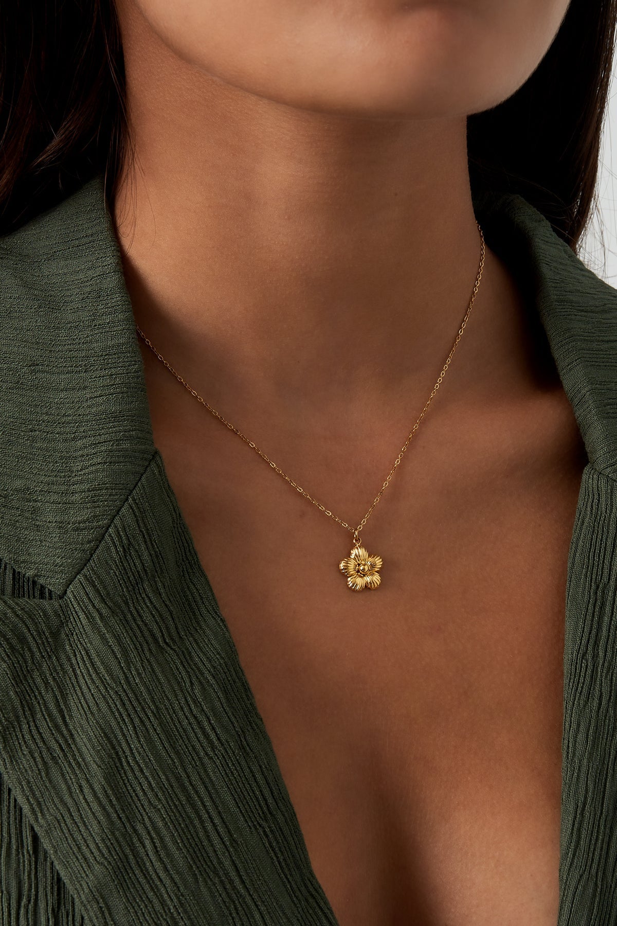 Model wearing gold flower pendant necklace paired with green outfit showing clavicle length fit