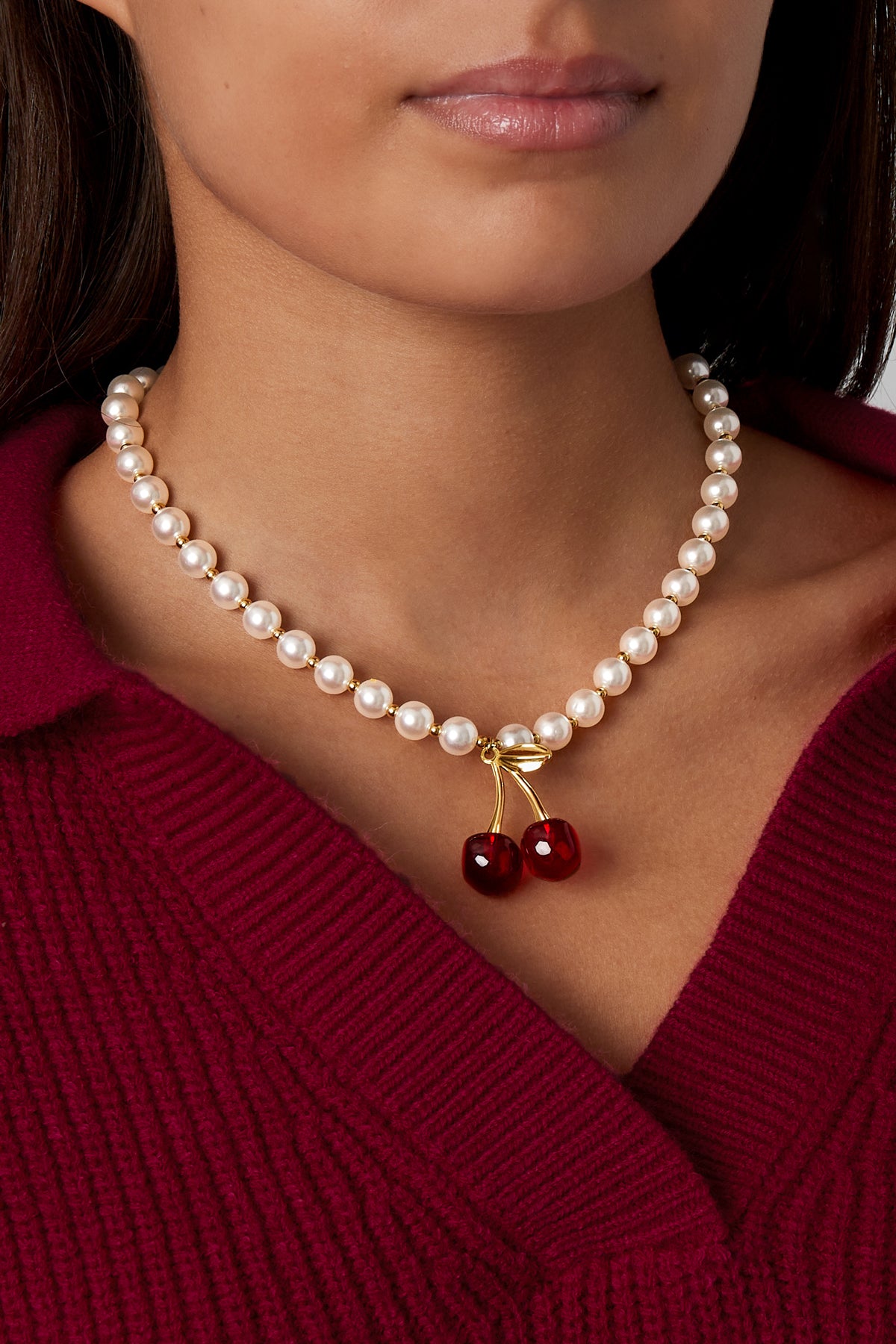 Model wearing pearl necklace with red cherry charm paired with burgundy top