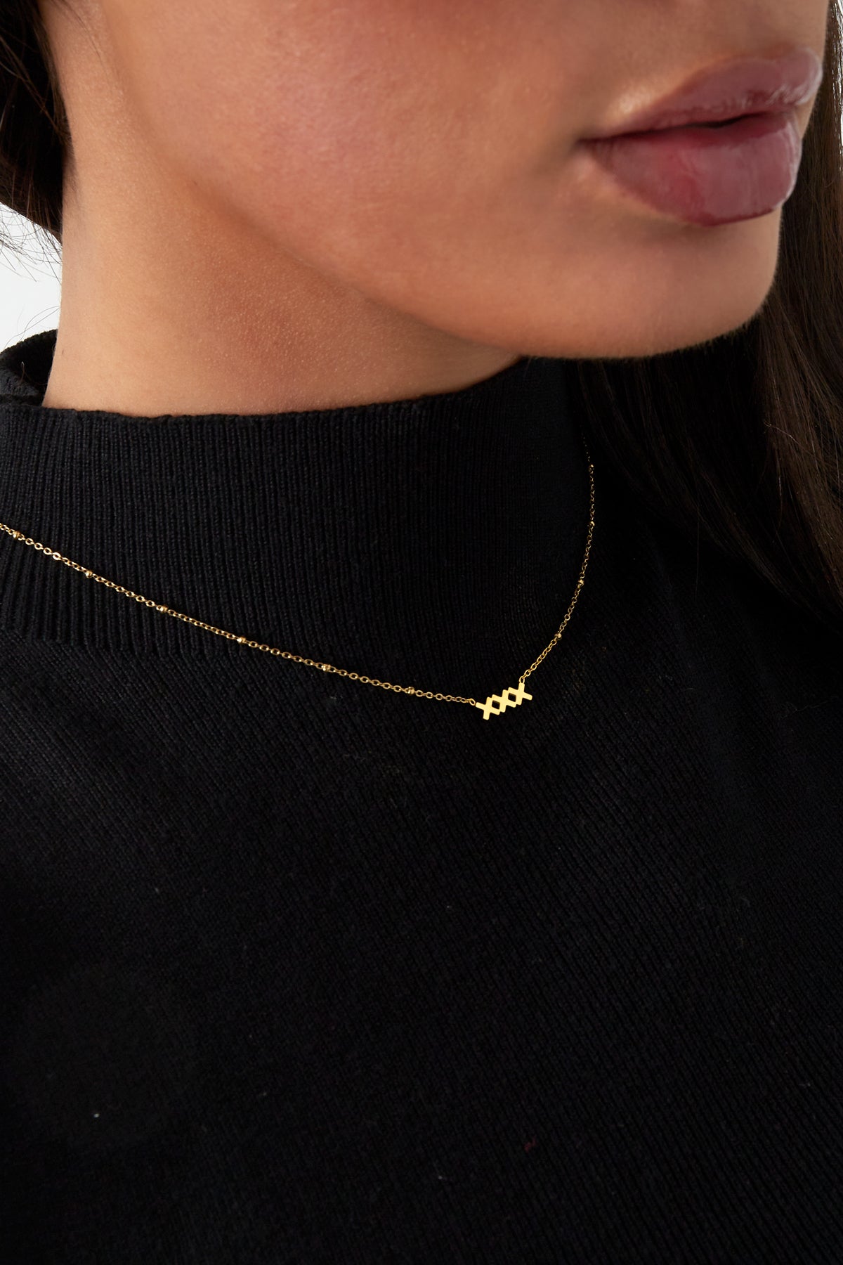 Close-up portrait of woman wearing gold XXX pendant necklace against black top