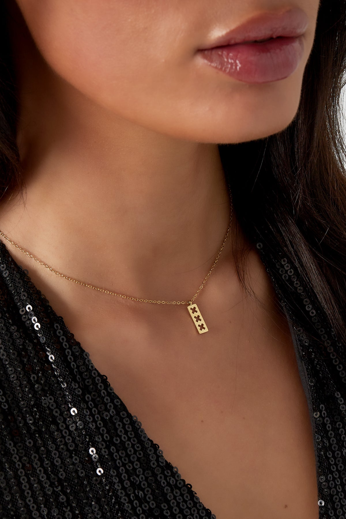 Close-up of a woman wearing the gold triple X pendant necklace paired with a black sequin top, showcasing necklace at clavicle length.
