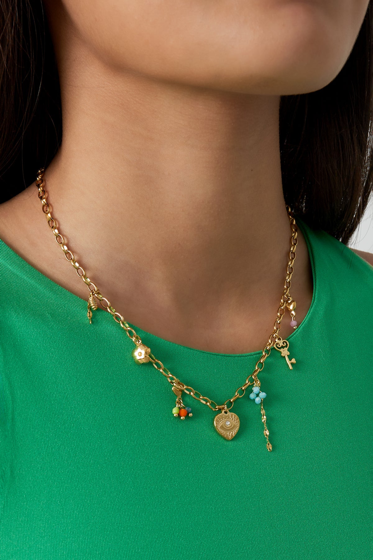 Model wearing golden charm link necklace with floral and key charms styled with a green top