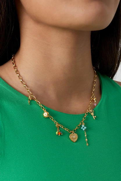 Model wearing golden charm link necklace with floral and key charms styled with a green top