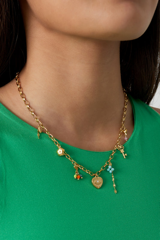 Model wearing golden charm link necklace with floral and key charms styled with a green top