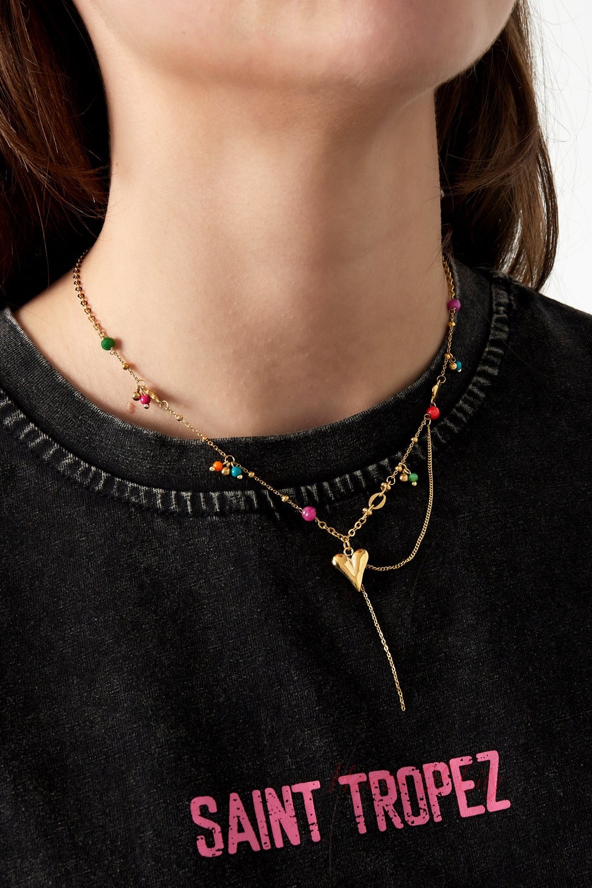 Model wearing playful gold heart pendant necklace with colourful beads over a black Saint Tropez t-shirt