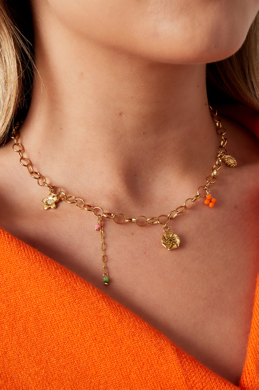 Close-up of necklace worn around a woman's neck with an orange top, showing detailed flower charms and beads