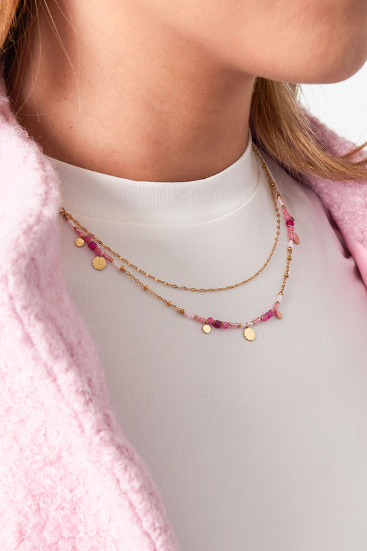 Model wearing a double layered necklace with gold chains and pink beads paired with a white top and pink jacket