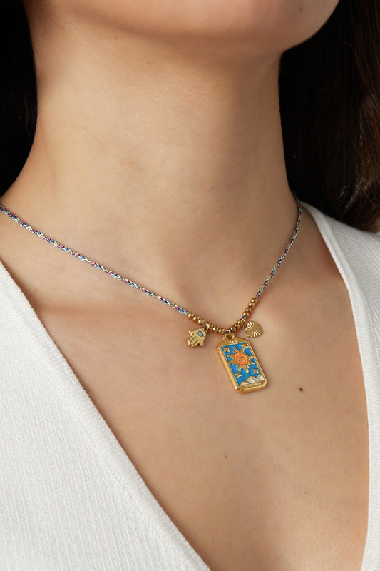 Model wearing braided necklace with gold sun, heart, and Hamsa hand charms against white top