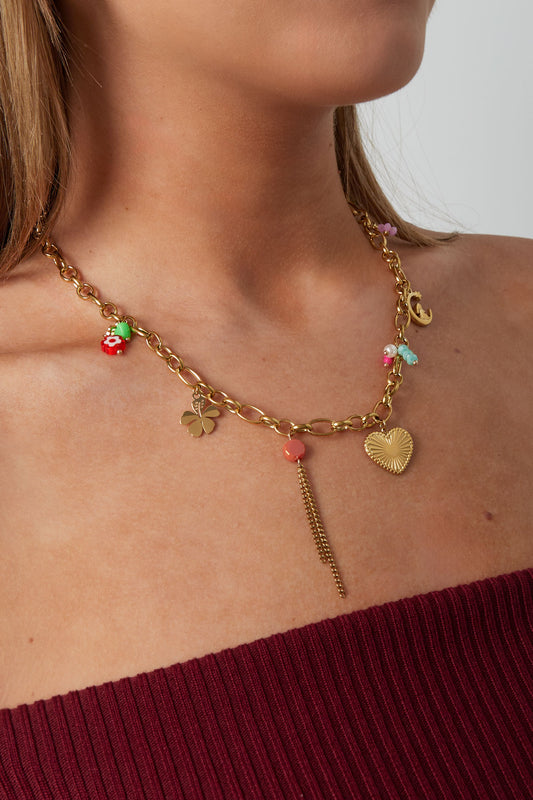 Model wearing gold charm chain necklace featuring heart pendant, moon and clover charms with colourful bead details, styled with burgundy top