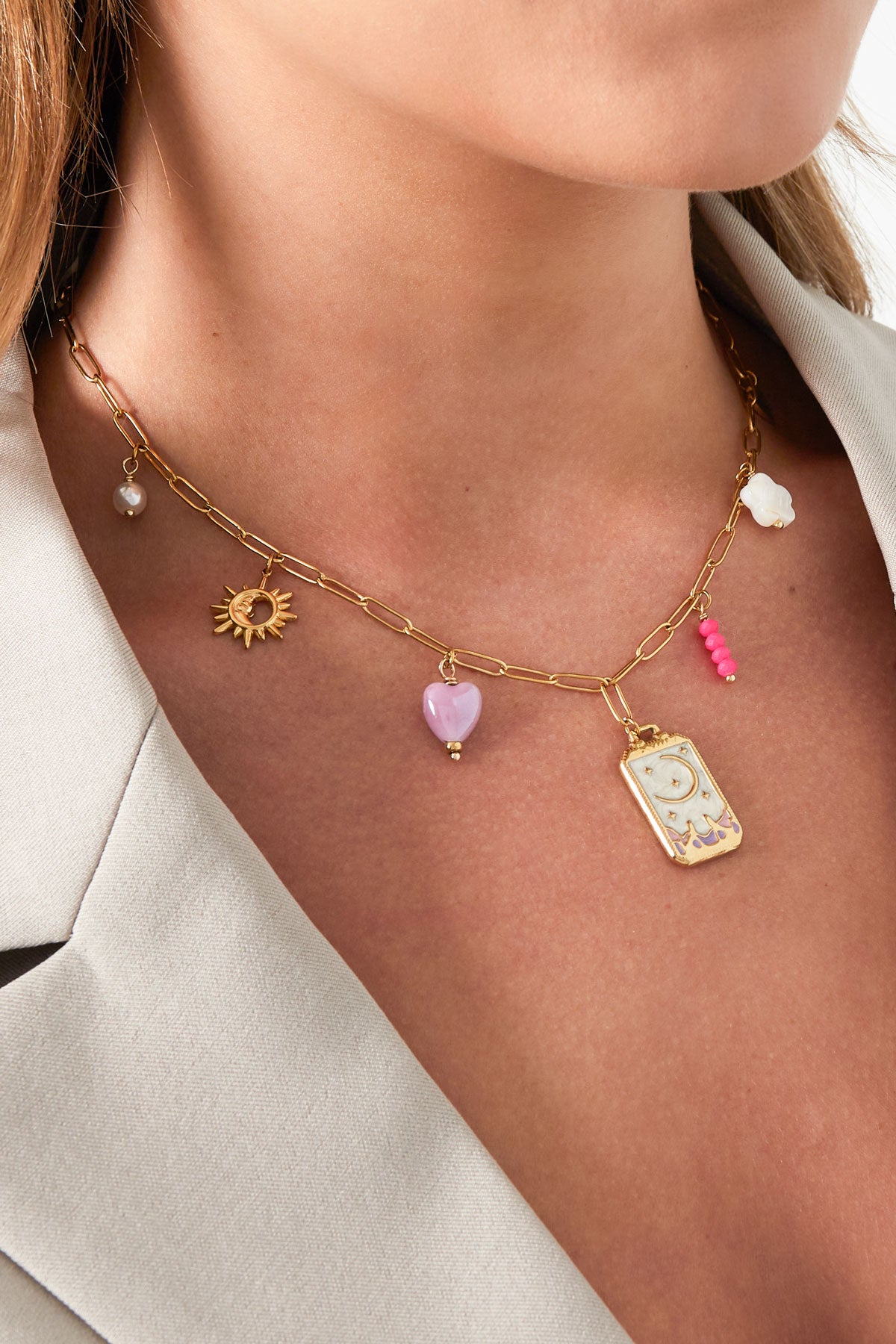Model wearing the gold-toned charm necklace showing charms close-up, styled with a light blazer