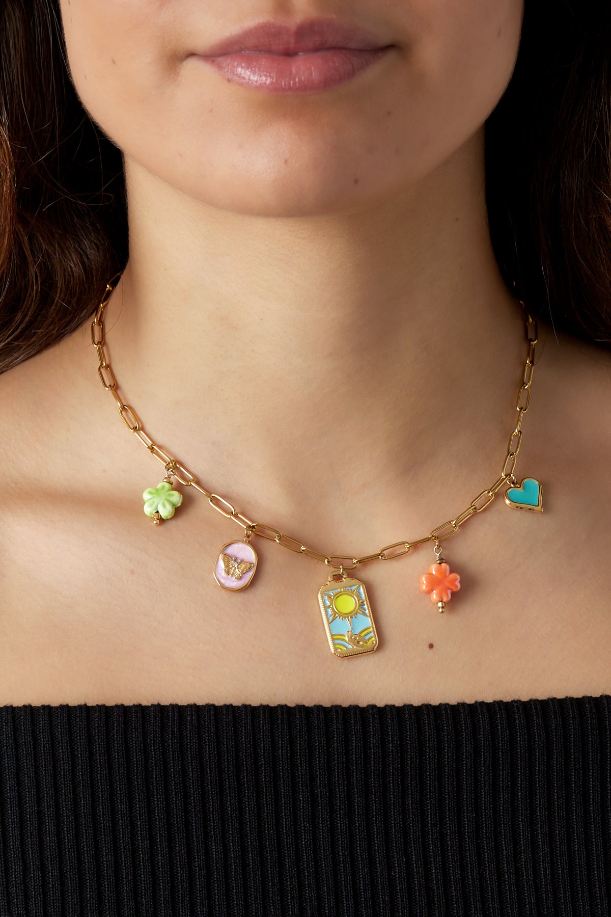 Close-up of a woman wearing the gold-tone charm link necklace with enamel charms showcasing playful and youthful design against a black top