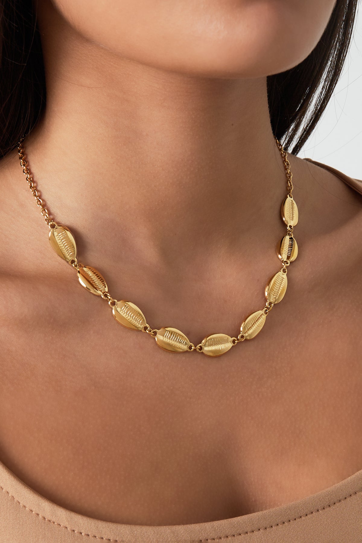 Woman wearing shell link gold chain necklace resting above her collarbone