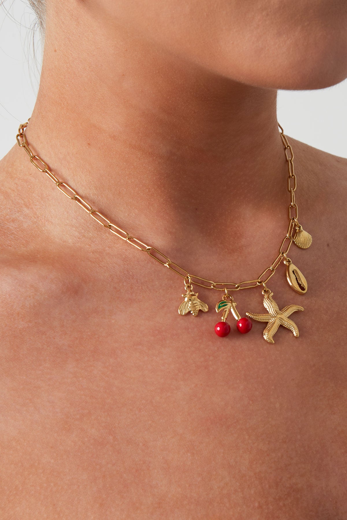 Model wearing gold charm necklace with beach-themed pendants showing close neck view