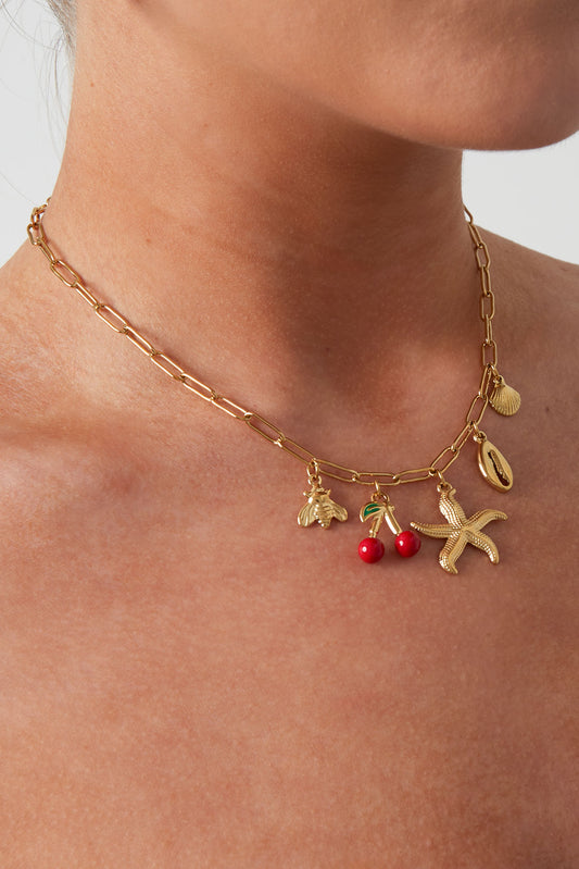 Model wearing gold charm necklace with beach-themed pendants showing close neck view