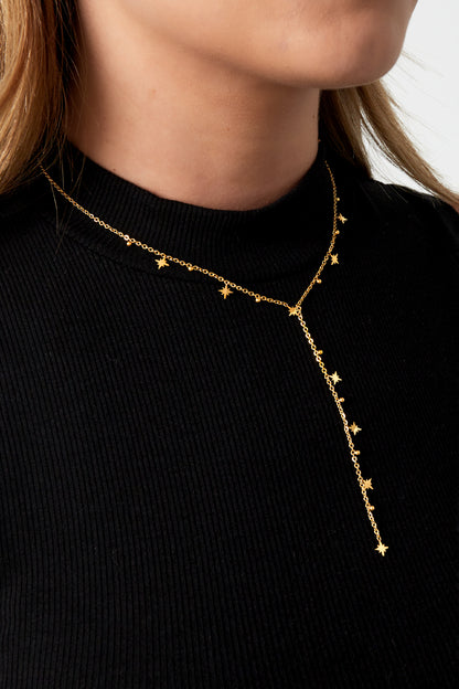 Model wearing the gold Twinkle Star Drop Necklace layered over a black ribbed top showing the star and bead details