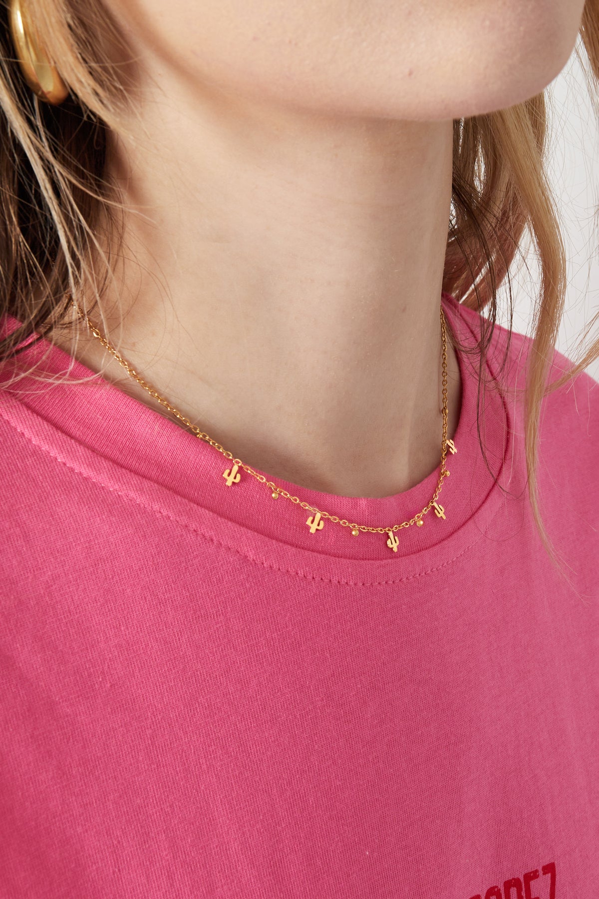 Close-up of a woman wearing the gold cactus charm necklace with a pink top