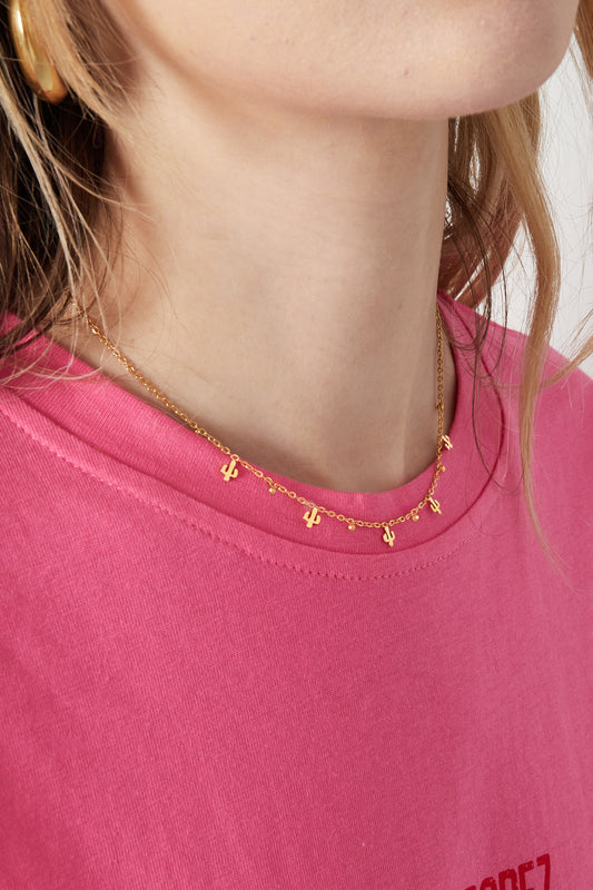 Close-up of a woman wearing the gold cactus charm necklace with a pink top