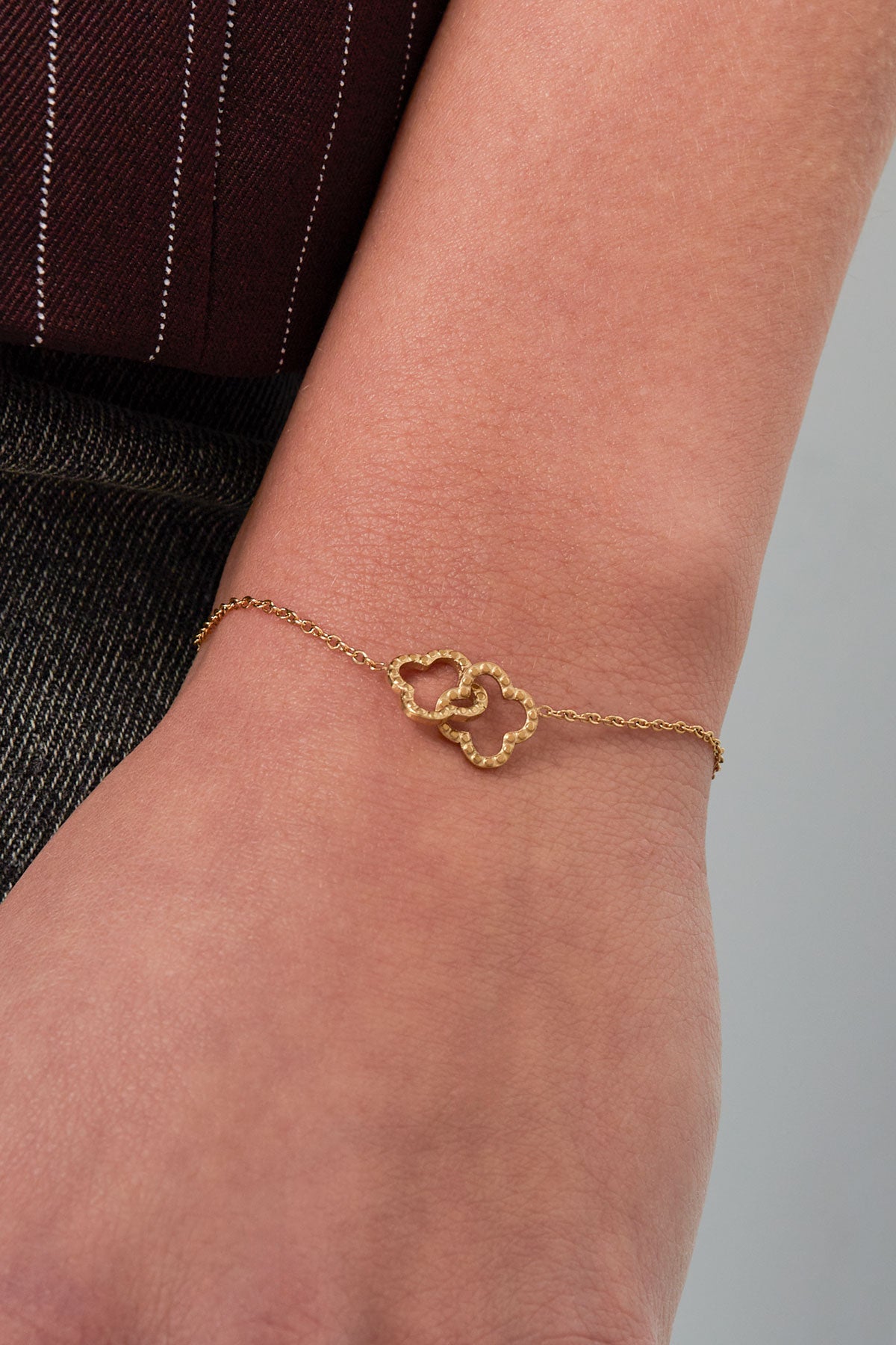 Close-up of the gold clover bracelet worn on a wrist, showing the hammered texture and delicate chain