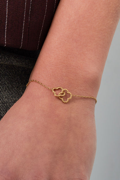 Close-up of the gold clover bracelet worn on a wrist, showing the hammered texture and delicate chain