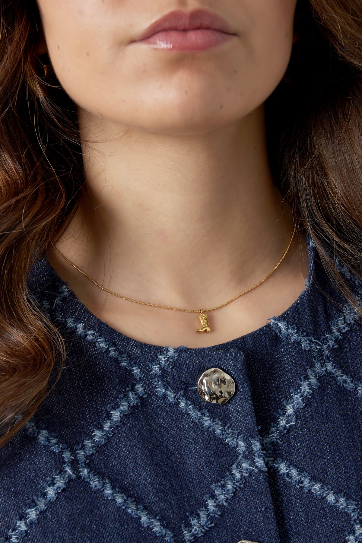 Close-up of a woman wearing the gold cowboy boot necklace paired with a blue textured jacket