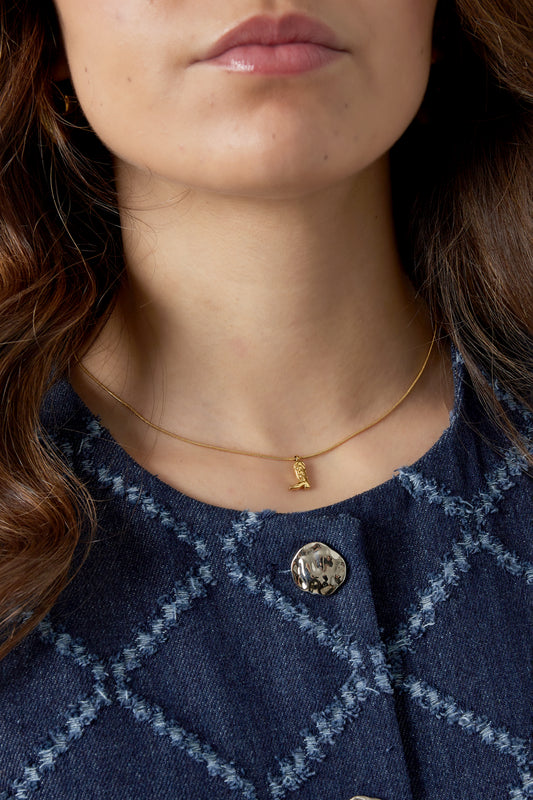 Close-up of a woman wearing the gold cowboy boot necklace paired with a blue textured jacket