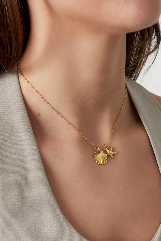 Close-up of woman wearing gold starfish and scallop shell charm necklace with beige top