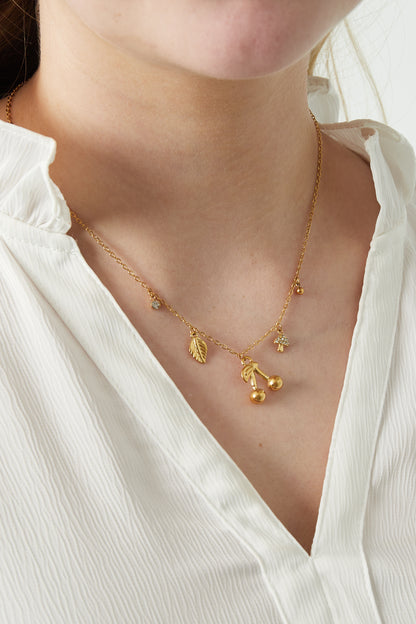 Close-up of a woman wearing a gold charm necklace with cherry and nature-inspired pendants paired with a white textured blouse