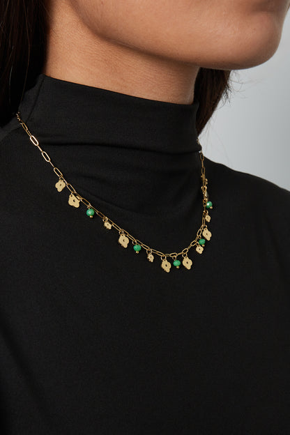 Model wearing the gold-tone clover charm necklace with green beads paired with a black top