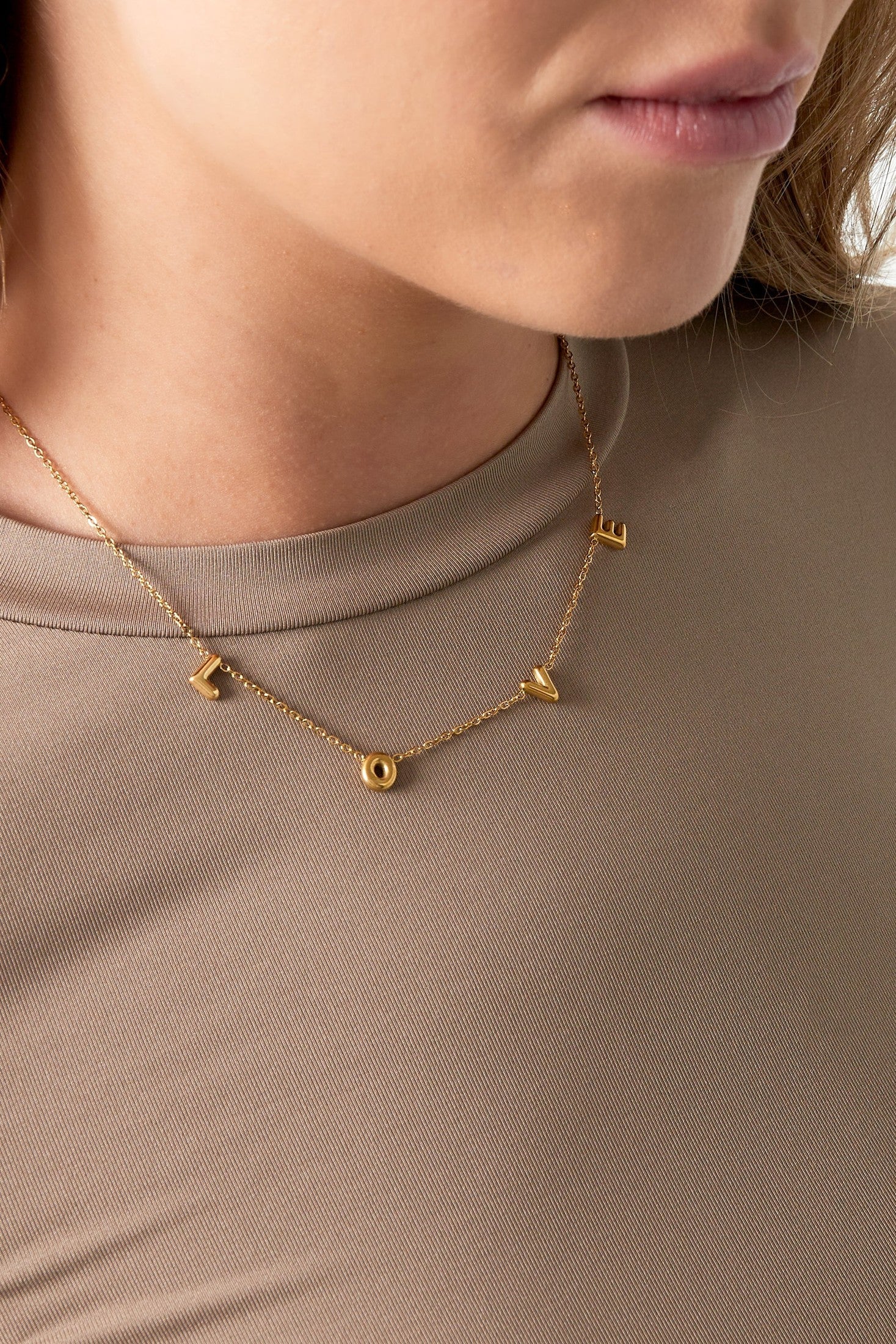 Close-up of woman wearing gold LOVE necklace paired with beige top