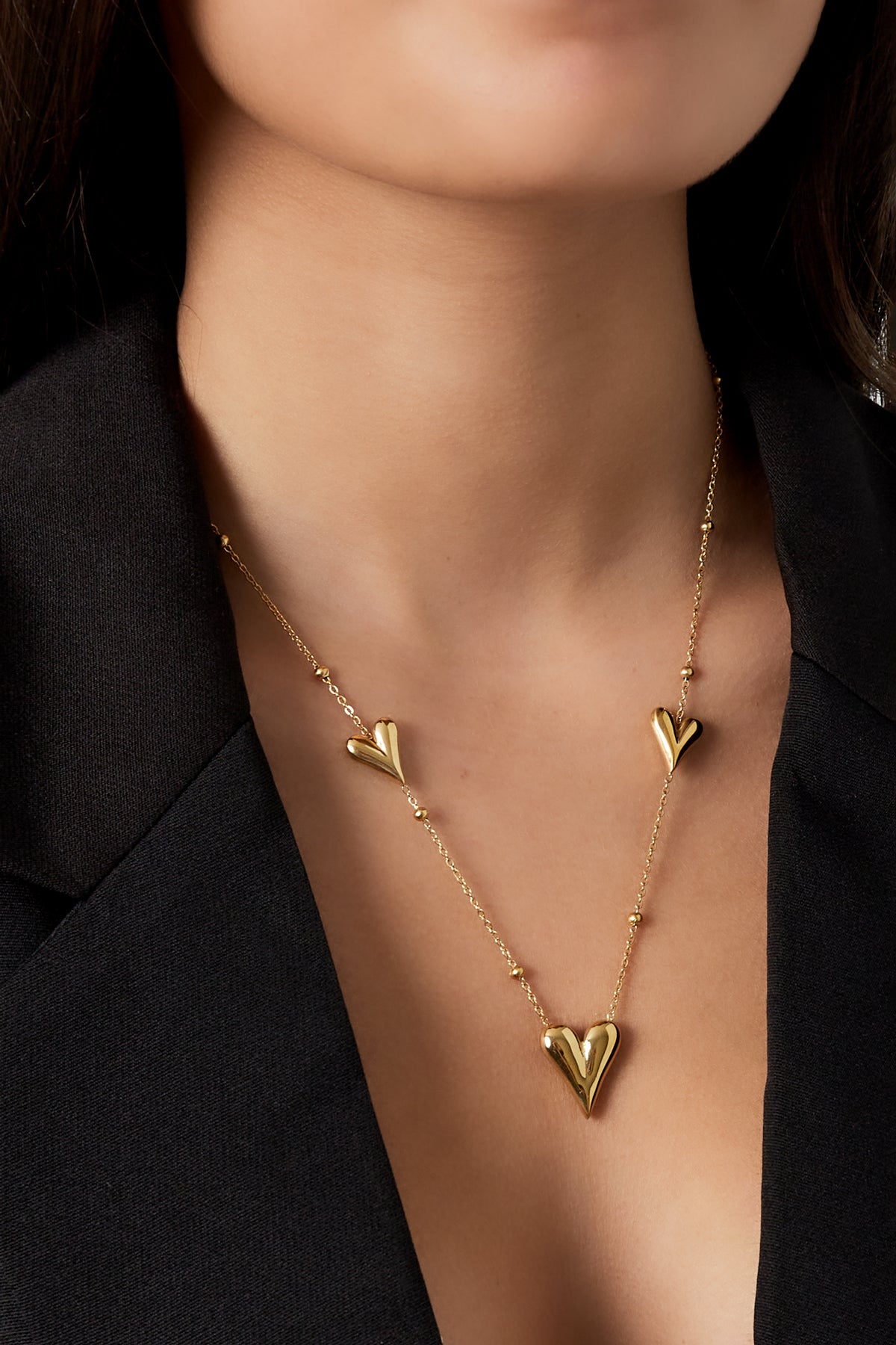 Close-up of a woman wearing the gold heart charm necklace with black blazer