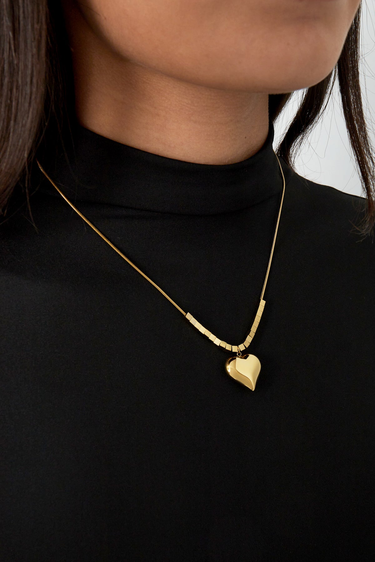 Gold chunky heart pendant necklace worn on a woman in black top showing stylish youthful look