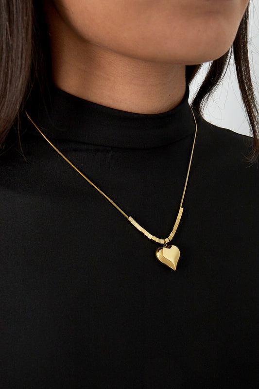 Gold chunky heart pendant necklace worn on a woman in black top showing stylish youthful look