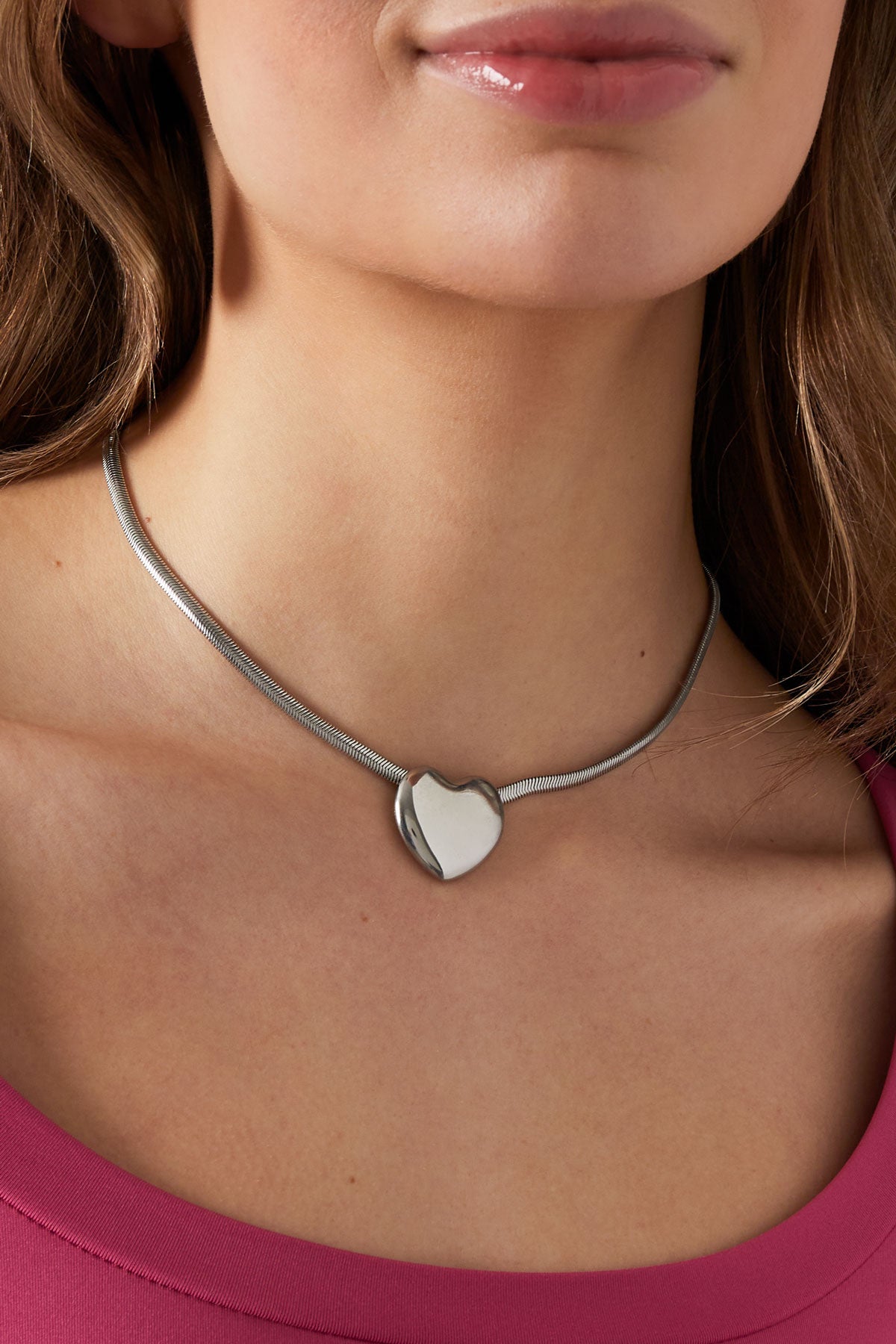 Silver-tone heart pendant necklace worn on a woman's neck with a pink top, showing soft shine and minimal style.