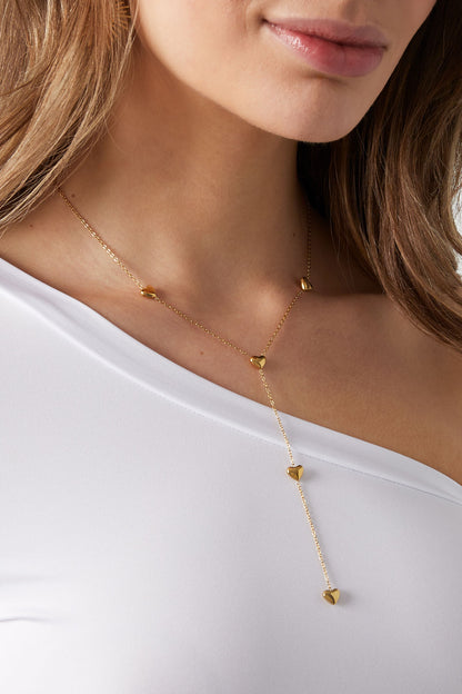 Close-up view of woman wearing gold heart drop necklace over white off-shoulder top