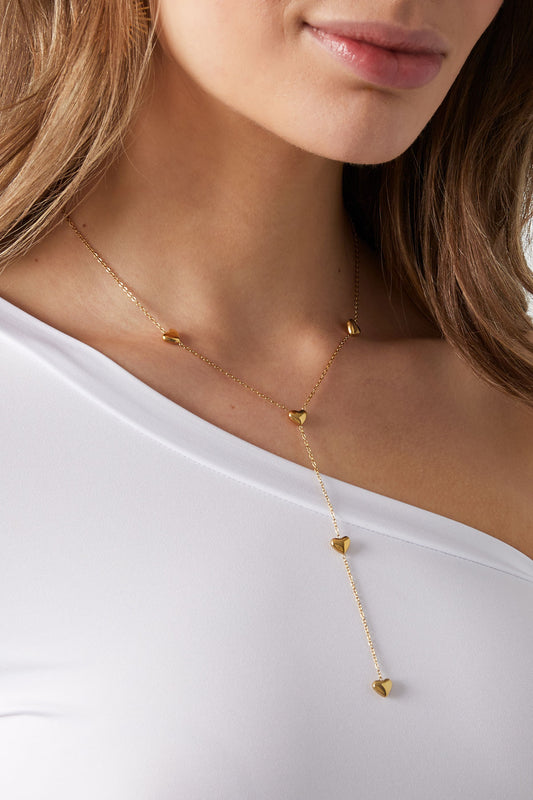Close-up view of woman wearing gold heart drop necklace over white off-shoulder top