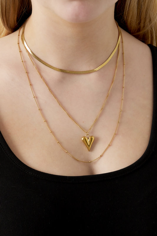 Woman wearing the gold layered necklace with heart pendant on a black top, highlighting the necklace's shine and texture