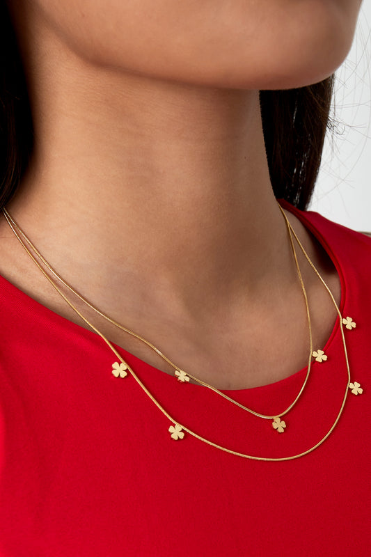 Close-up of woman wearing double-layer gold clover necklace over a red top highlighting youthful minimal style