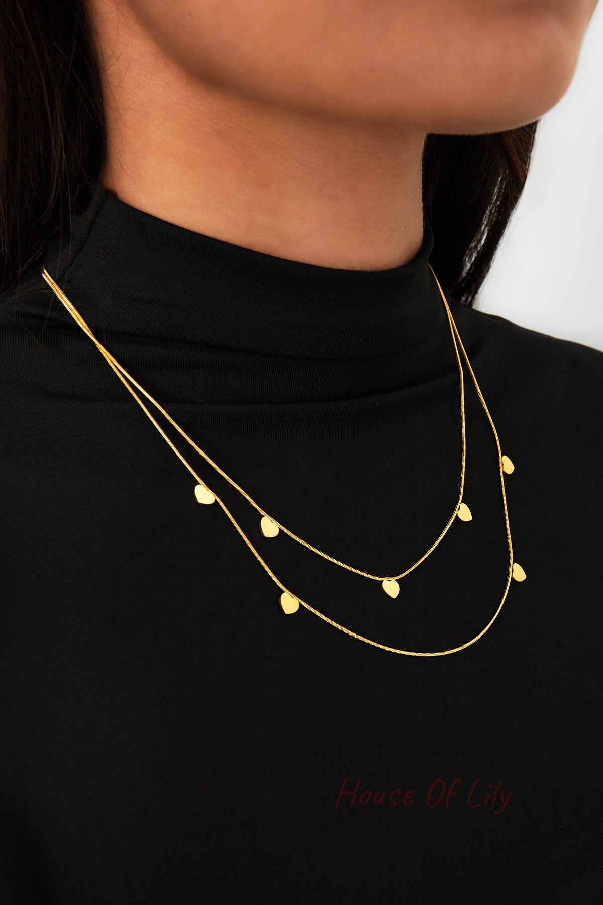 Close-up on woman wearing gold double-layered necklace with small hearts over black turtleneck