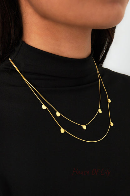 Close-up on woman wearing gold double-layered necklace with small hearts over black turtleneck