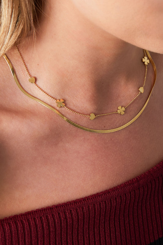 Model wearing gold layered necklace featuring hearts and clovers paired with a burgundy top