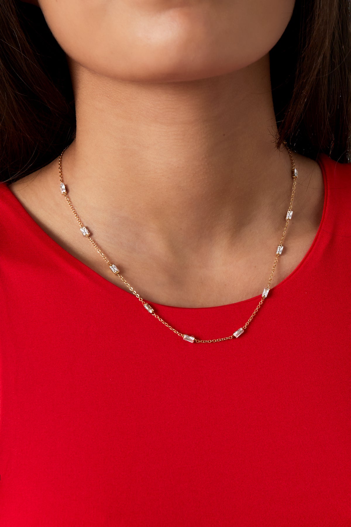 Model wearing the gold crystal chain necklace paired with a vibrant red top, showcasing elegant collarbone fit