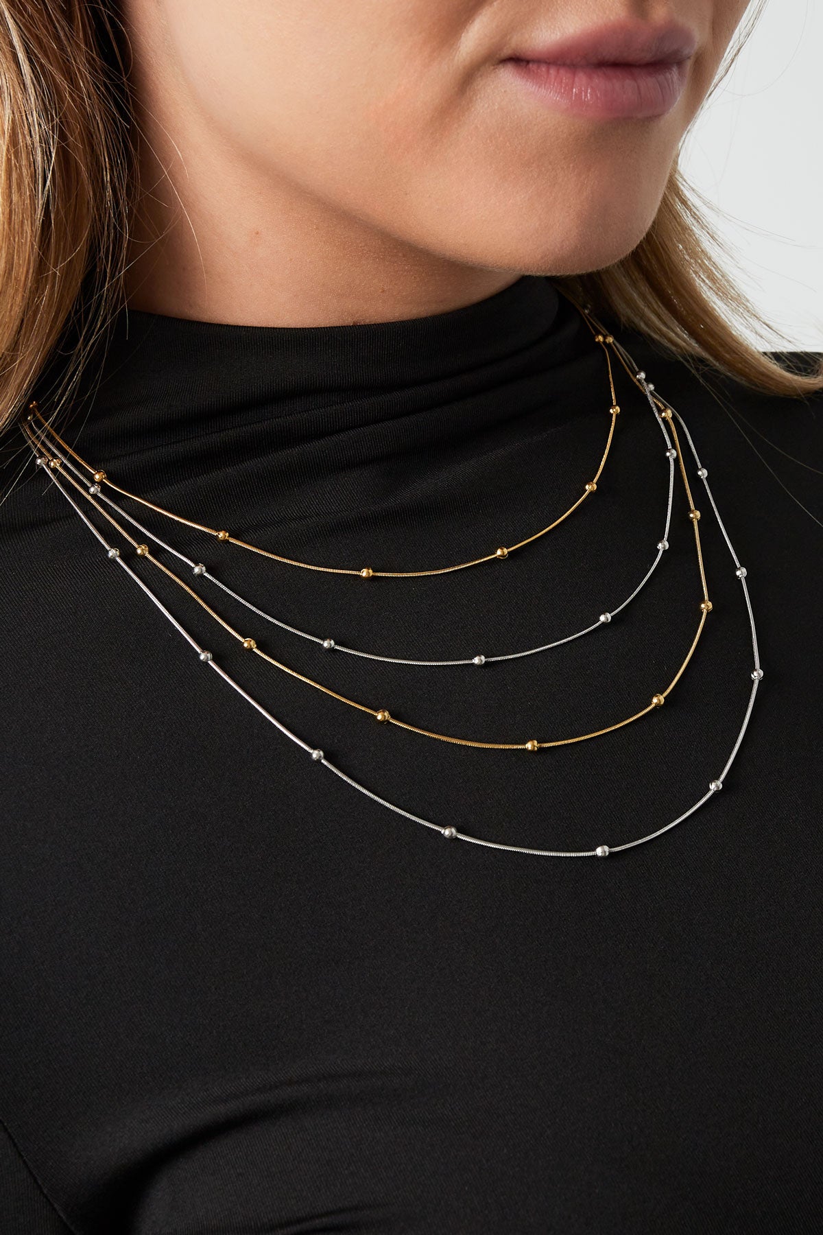 Woman wearing layered mixed gold and silver beaded necklaces on black top