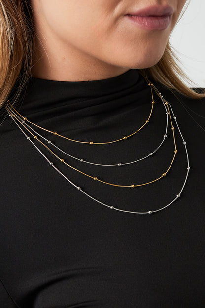 Woman wearing layered mixed gold and silver beaded necklaces on black top