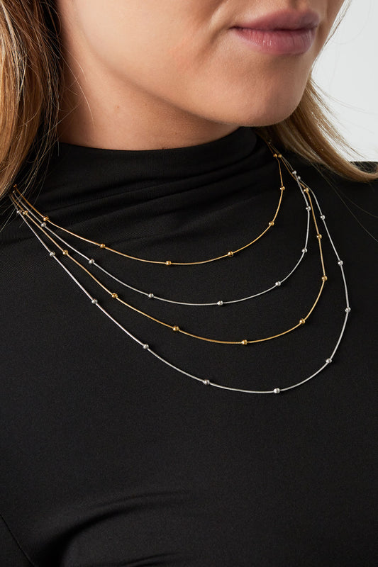 Woman wearing layered mixed gold and silver beaded necklaces on black top