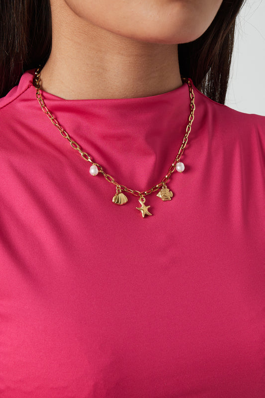 Close-up of woman wearing gold beach charm necklace with starfish, shell, fish pendants and pearls over bright pink top